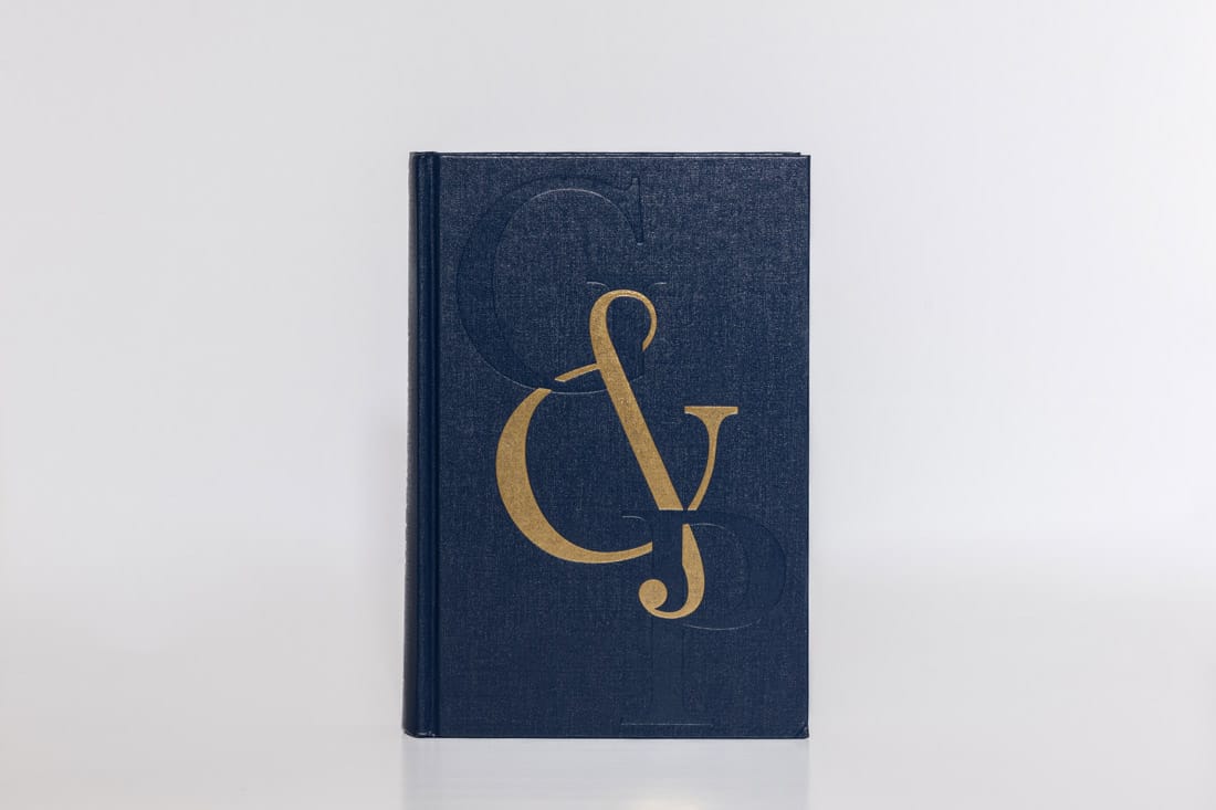 Navy blue linen hardcover book featuring blind embossed ampersand design with gold foil stamping overlay, showcasing combined embossing and foil techniques.