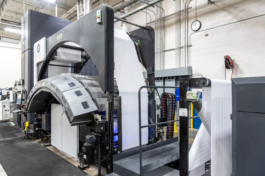 HP T360 mono digital printer with curved paper feed system in industrial print facility with exposed ceiling and concrete floors.