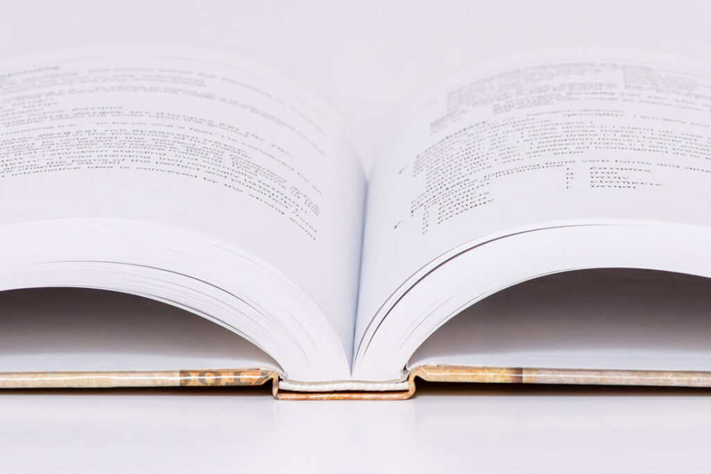 Open case bound book laying flat at 180 degrees, showing marbled brown and gold spine with white pages demonstrating lay-flat binding capability.