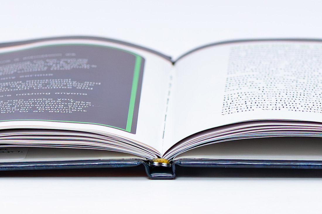 Open hardcover book showing lay-flat binding with gray and white pages featuring printed text.