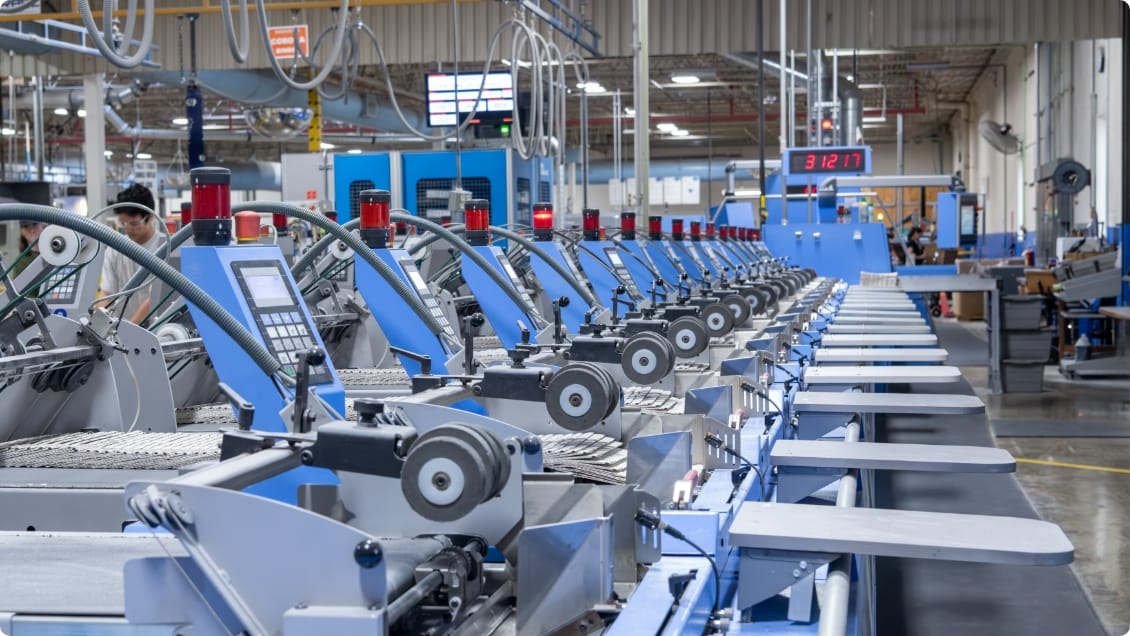 Row of blue and gray book binding machines with red indicators actively binding books in print manufacturing facility.
