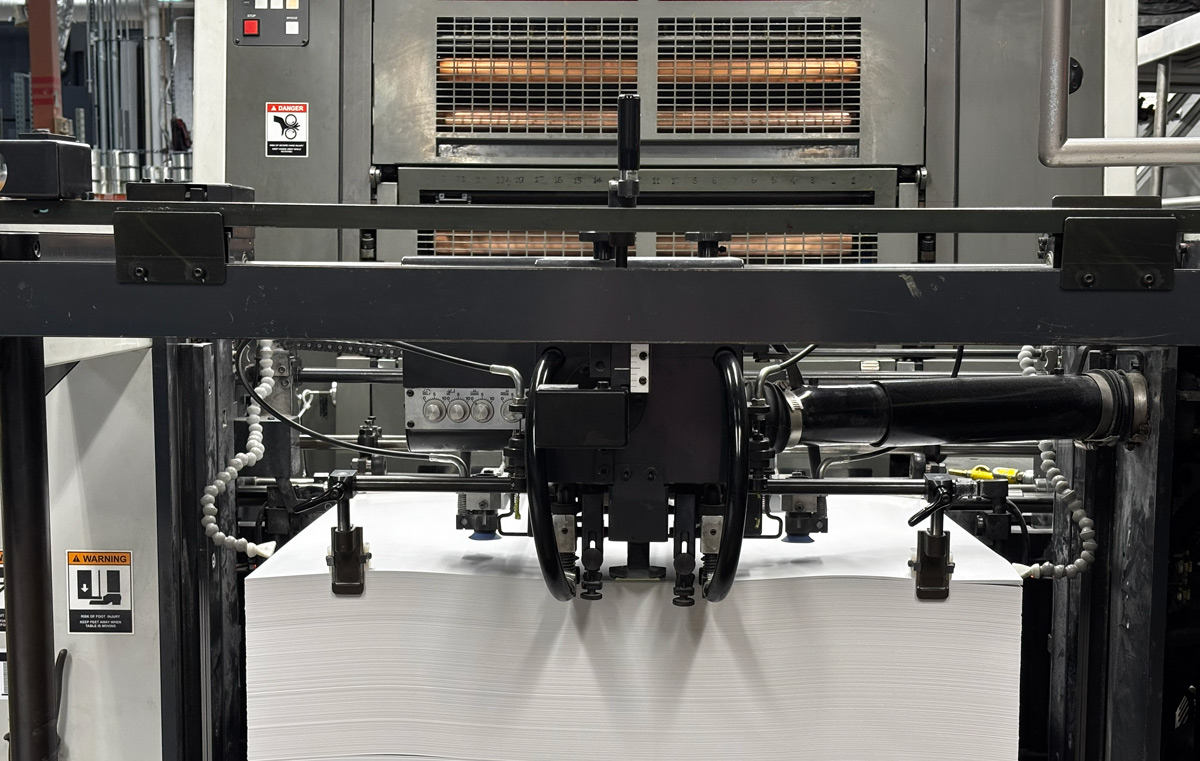 Sheet-fed printer with automated paper feed system and delivery tray in print manufacturing facility.
